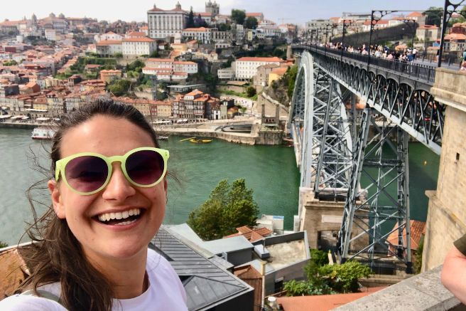 Nicola wears lime green sunglasses and smiles in front of the Porto Bridge